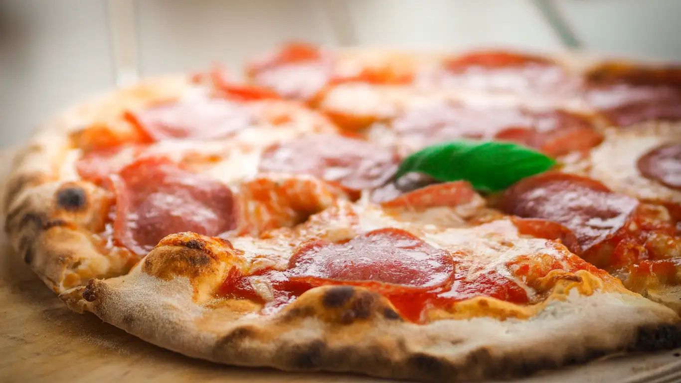 En glutenfri pepperoni-pizza med sprød skorpe, smeltet ost, tomatsauce og et frisk basilikumblad på toppen.